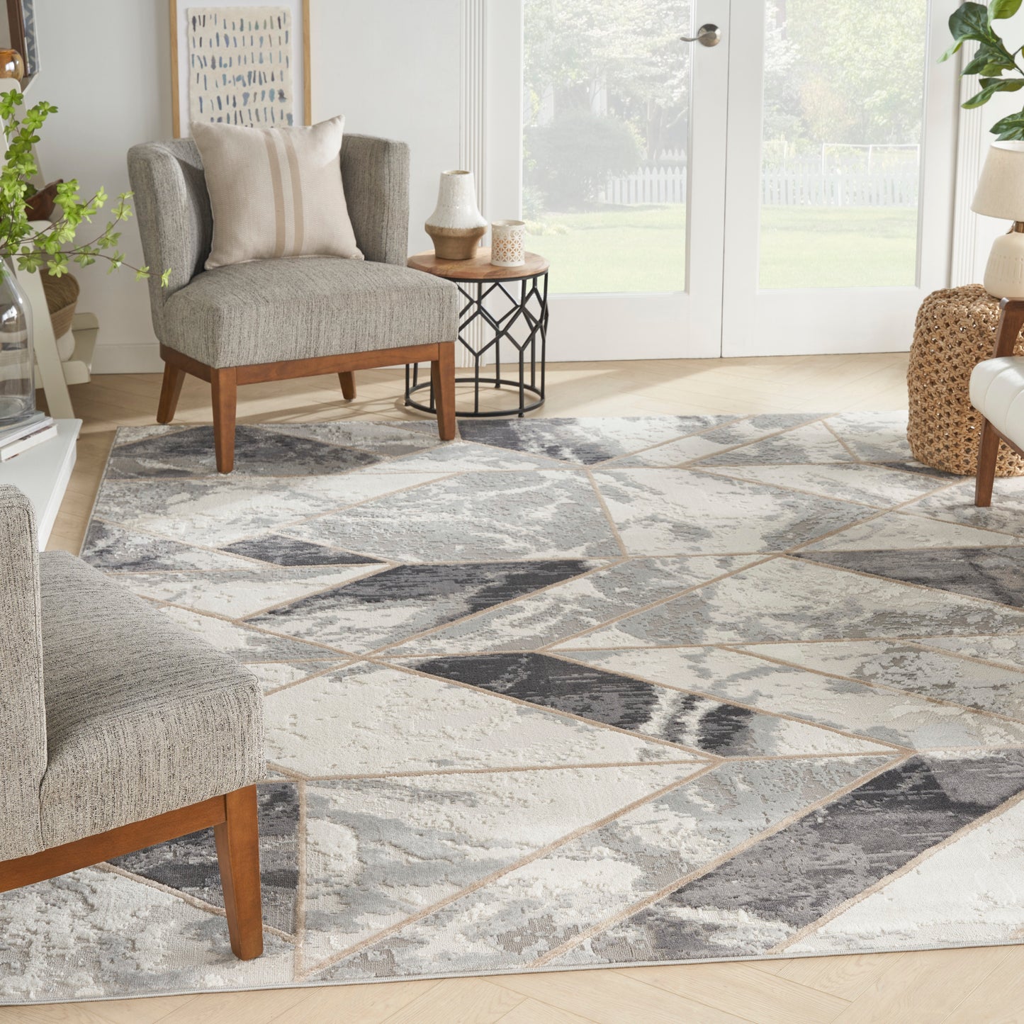 Living room with a geometric gray-beige rug, gray chairs with wood legs, side table, plants, and glass doors.