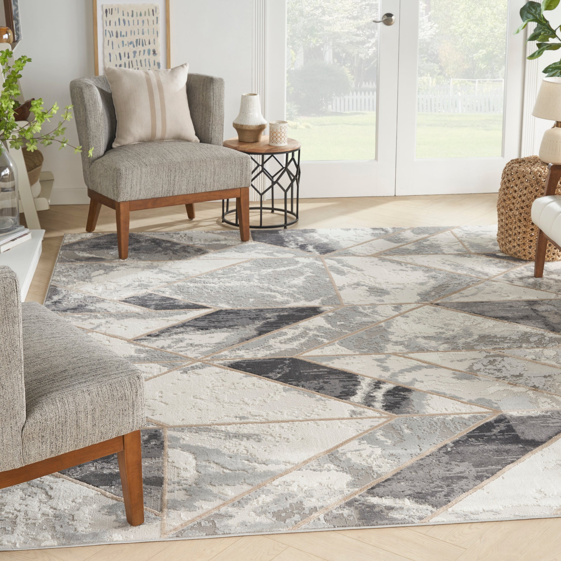 Living room with a geometric gray-beige rug, gray chairs with wood legs, side table, plants, and glass doors.