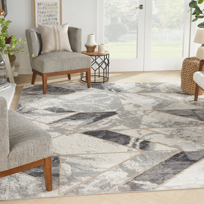 Living room with a geometric gray-beige rug, gray chairs with wood legs, side table, plants, and glass doors.