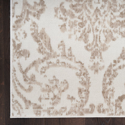 Corner view of a beige damask-pattern rug with light brown floral scrolls on a dark wood floor.