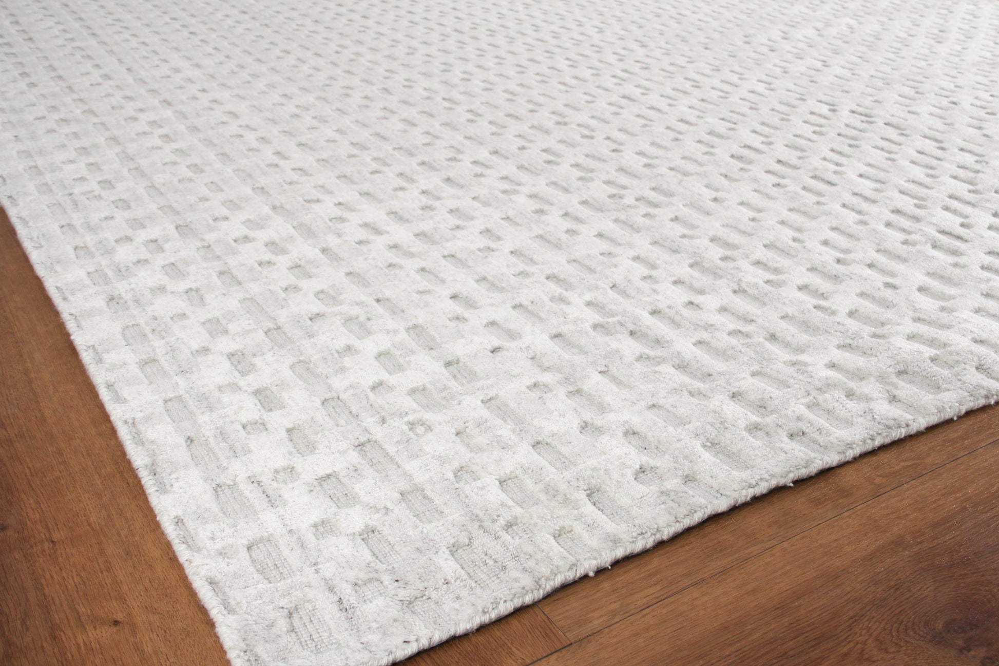 Cream textured rug with a raised square-grid pattern on a wooden floor.