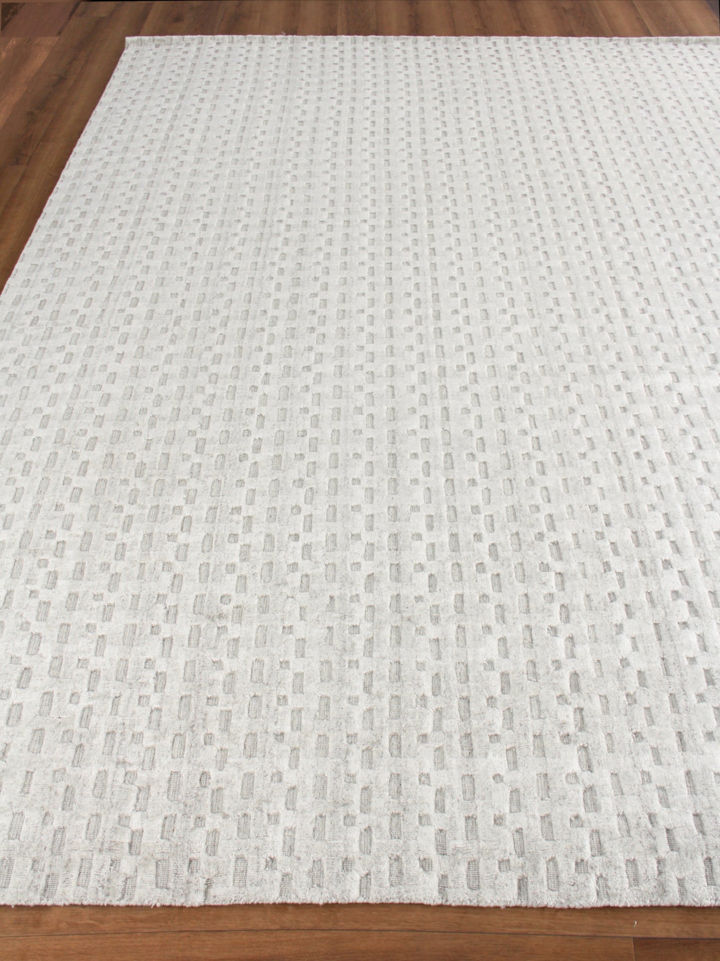 Rectangular light gray woven rug with a raised dotted rectangular pattern on hardwood floor