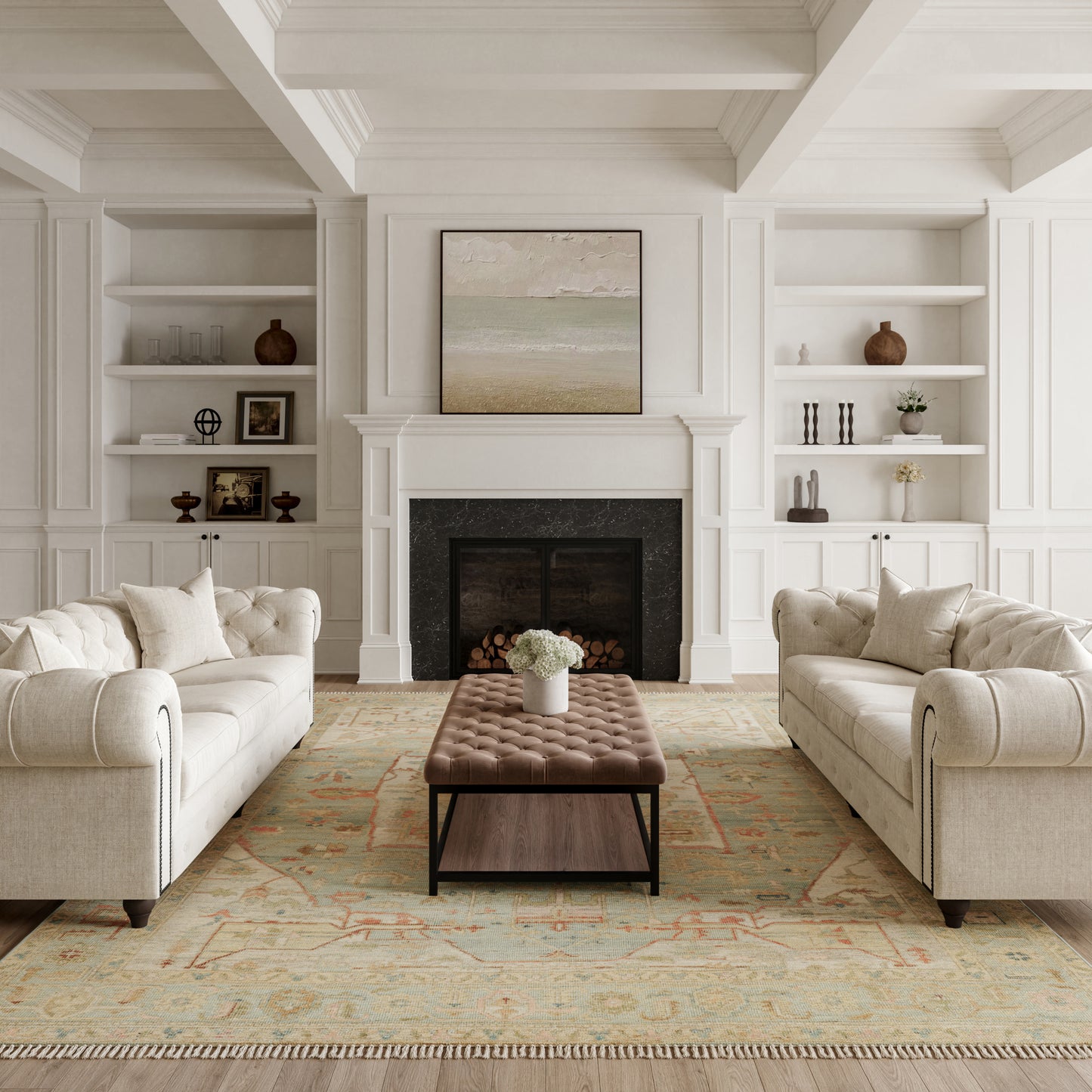 White paneled living room with fireplace, built-in shelves, beige tufted sofas, brown tufted ottoman, pastel rug.