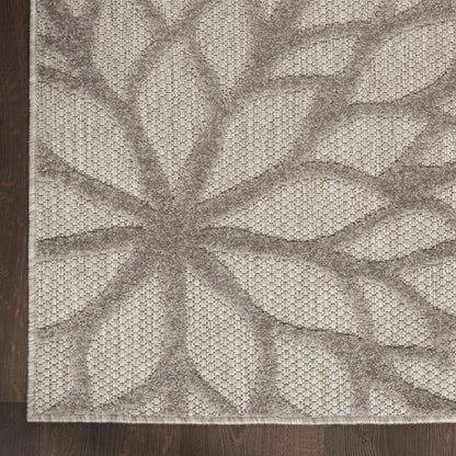 Beige and taupe textured rug with a large leaf/starburst pattern and a fringed edge on dark wood floor.