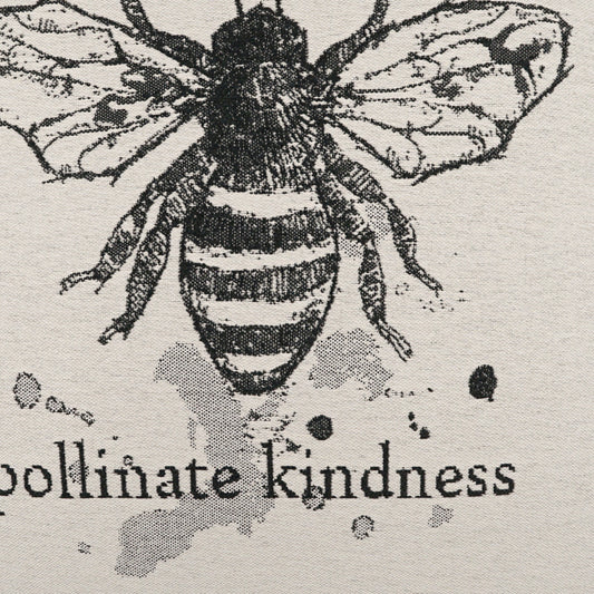 Vintage black bee illustration on beige fabric with ink splatters and the words pollinate kindness.