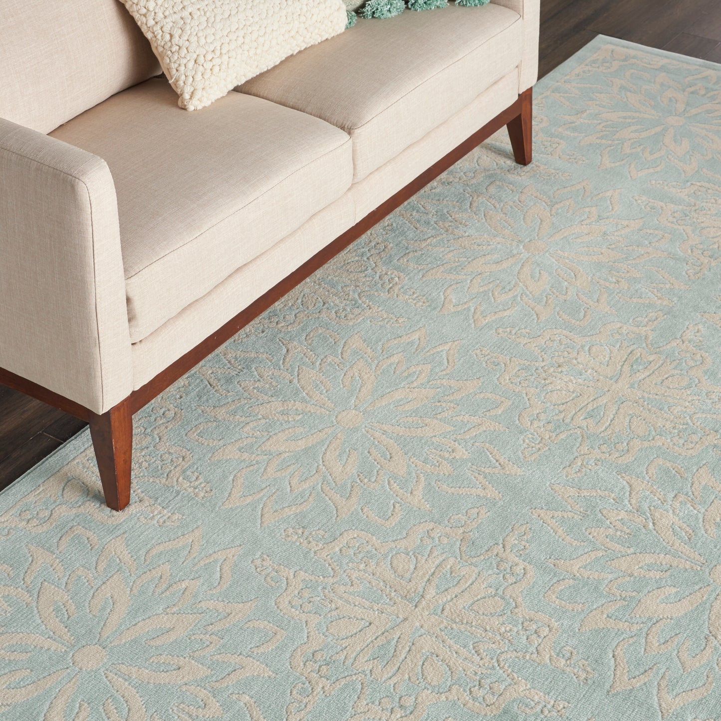 Pale blue rug with cream floral damask beneath a light beige mid-century sofa on wooden legs.