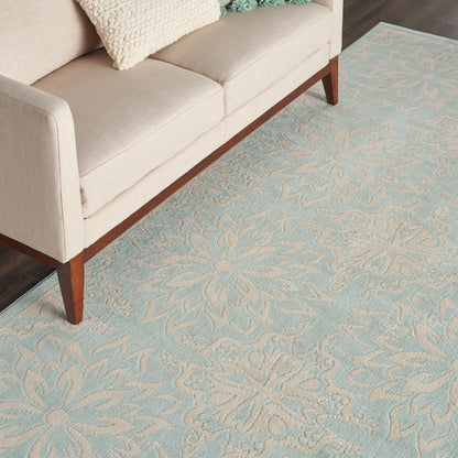 Pale blue rug with cream floral damask beneath a light beige mid-century sofa on wooden legs.