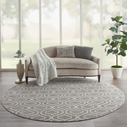 Round gray rug with white swirl under beige sofa; knitted throw, two pillows, gold side table, potted plant by window.