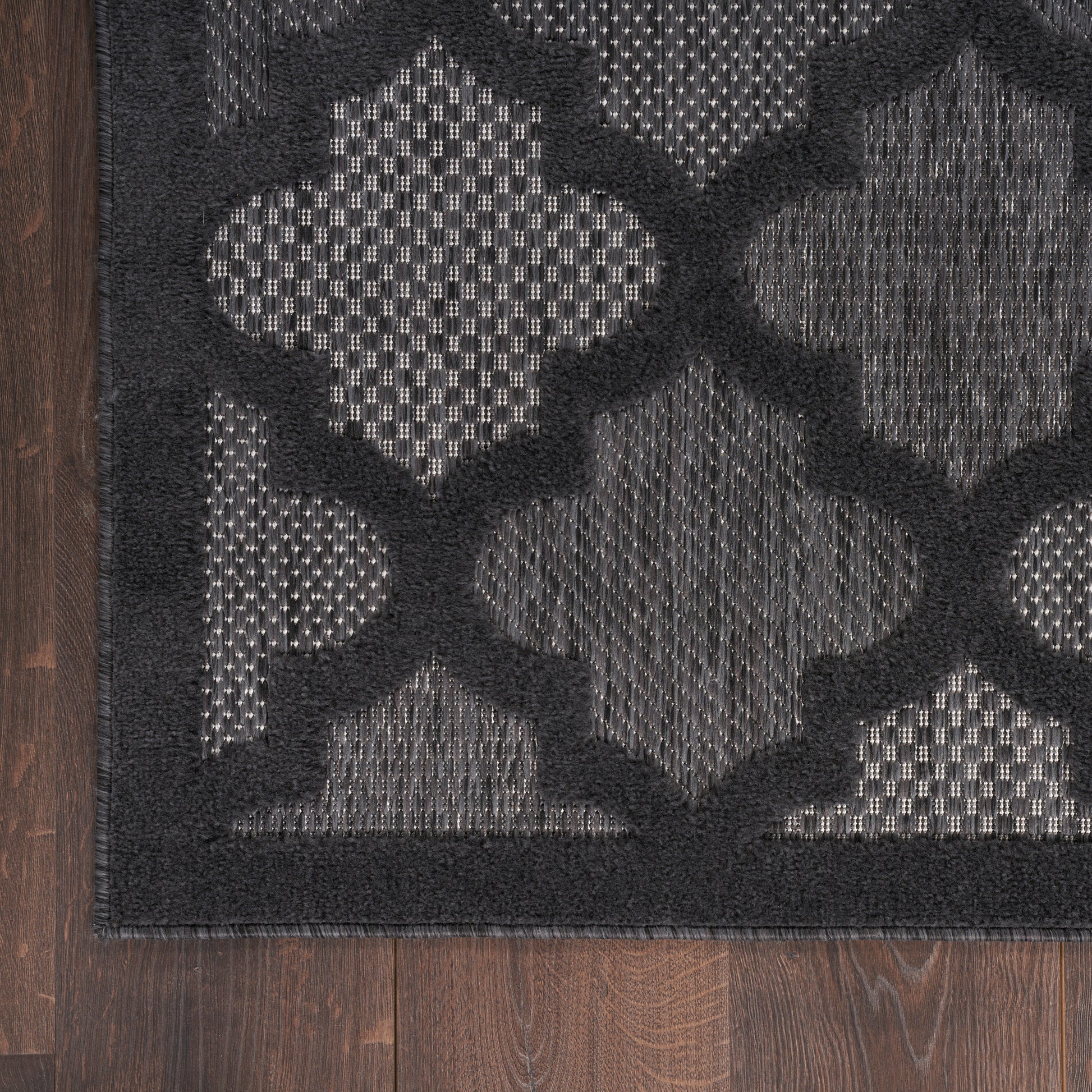 Charcoal and black flatwoven rug with bold lattice quatrefoil pattern and dark border.