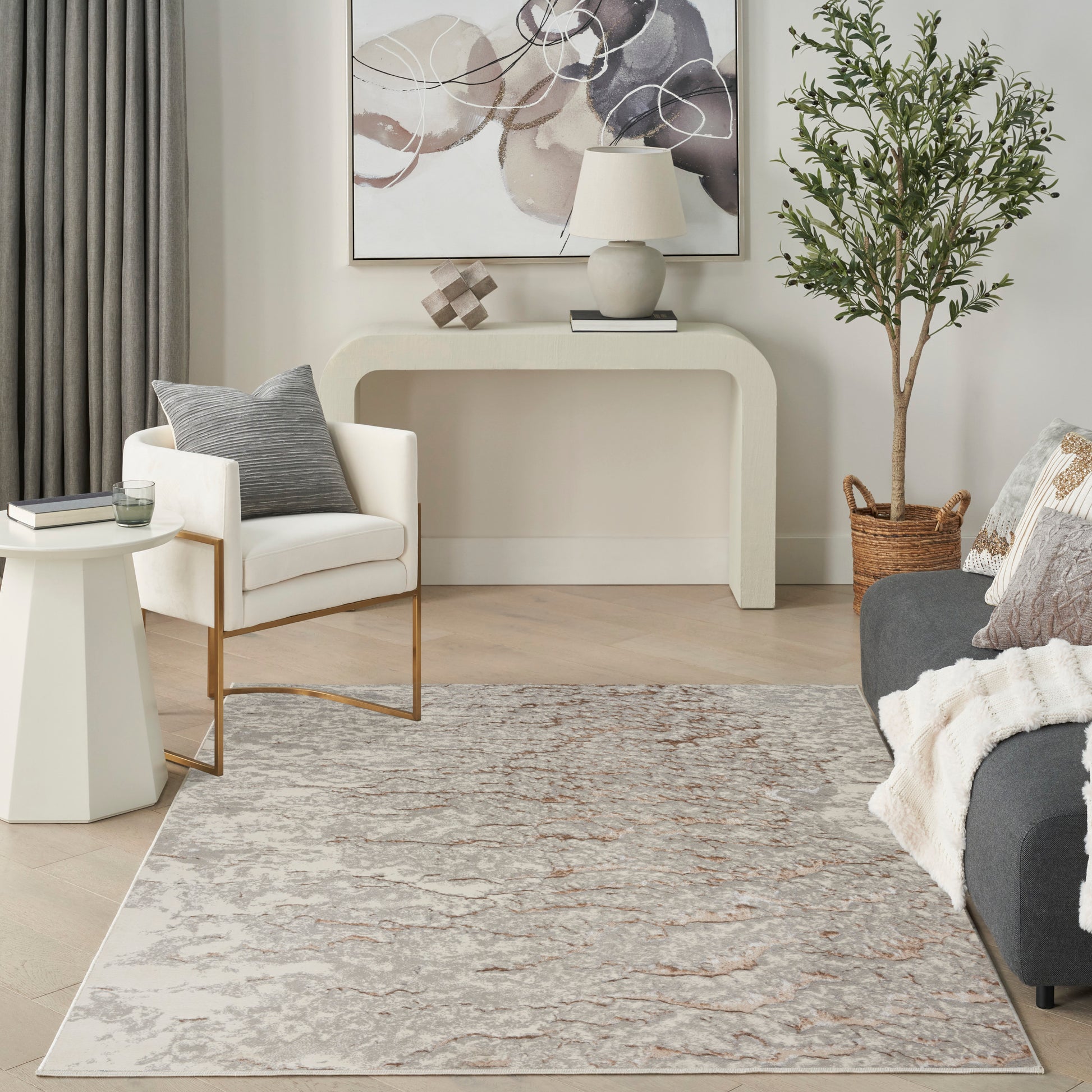 Neutral, modern living room with curved cream console, abstract art, cream armchair, gray sofa, plant in basket, beige rug.