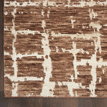 Brown and cream geometric area rug with cream linear patterns and plush pile on dark wood floor.