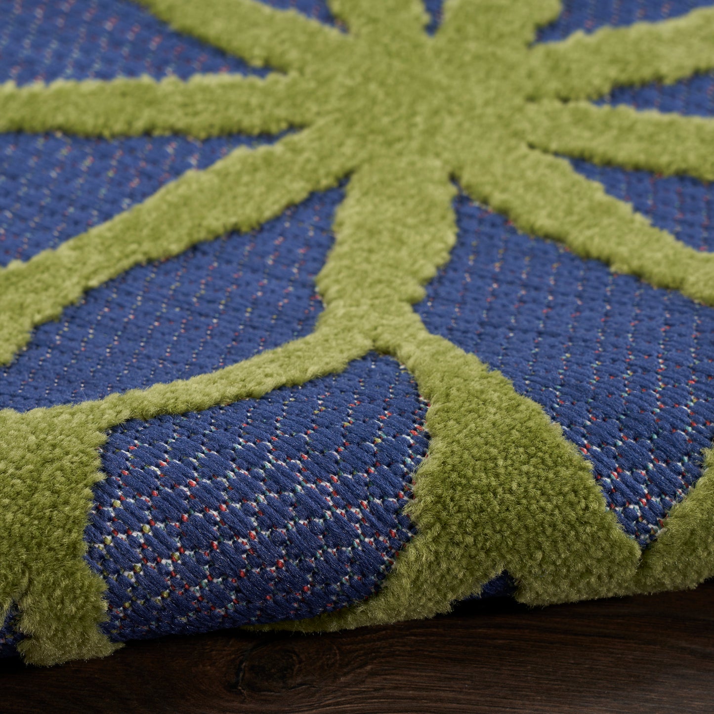 Close-up of blue woven rug with lime green raised geometric pattern on dark wood floor.