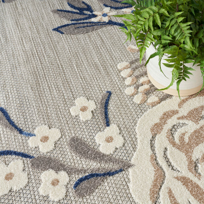 Beige woven rug with cream flowers and blue stems; plant in white pot at edge.