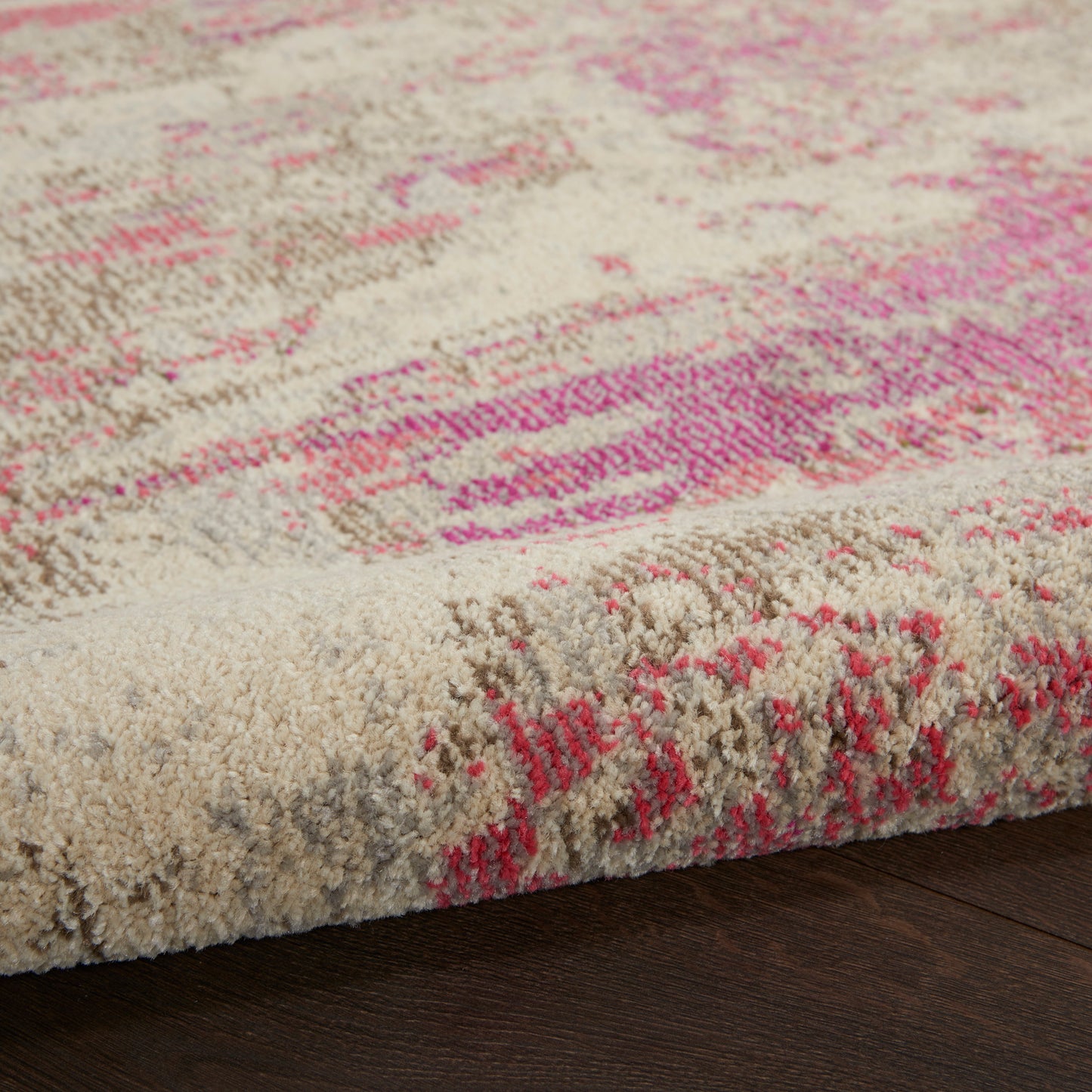 Beige plush area rug with pink abstract pattern; tufted pile and visible edge on dark wood floor, contemporary style.