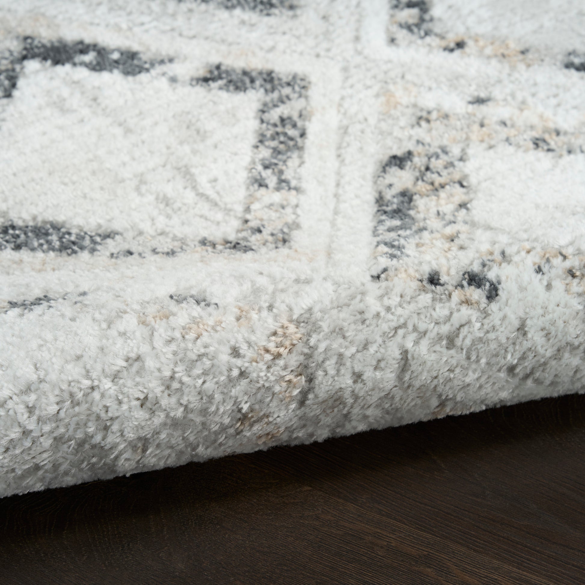 Plush cream rug with gray geometric pattern and rolled edge on dark wood floor.