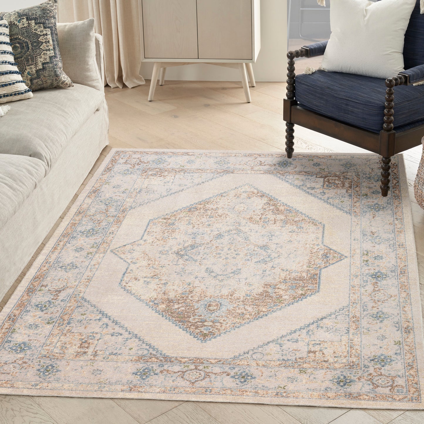 Cream woven area rug with pale blue and tan medallion pattern in a living room with a sofa and navy chair.