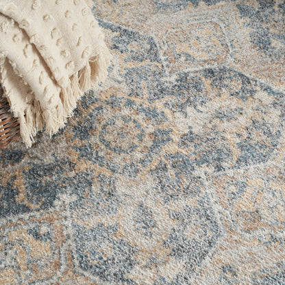 Cream fringed throw draped over a wicker basket on a blue-beige ornate distressed area rug.