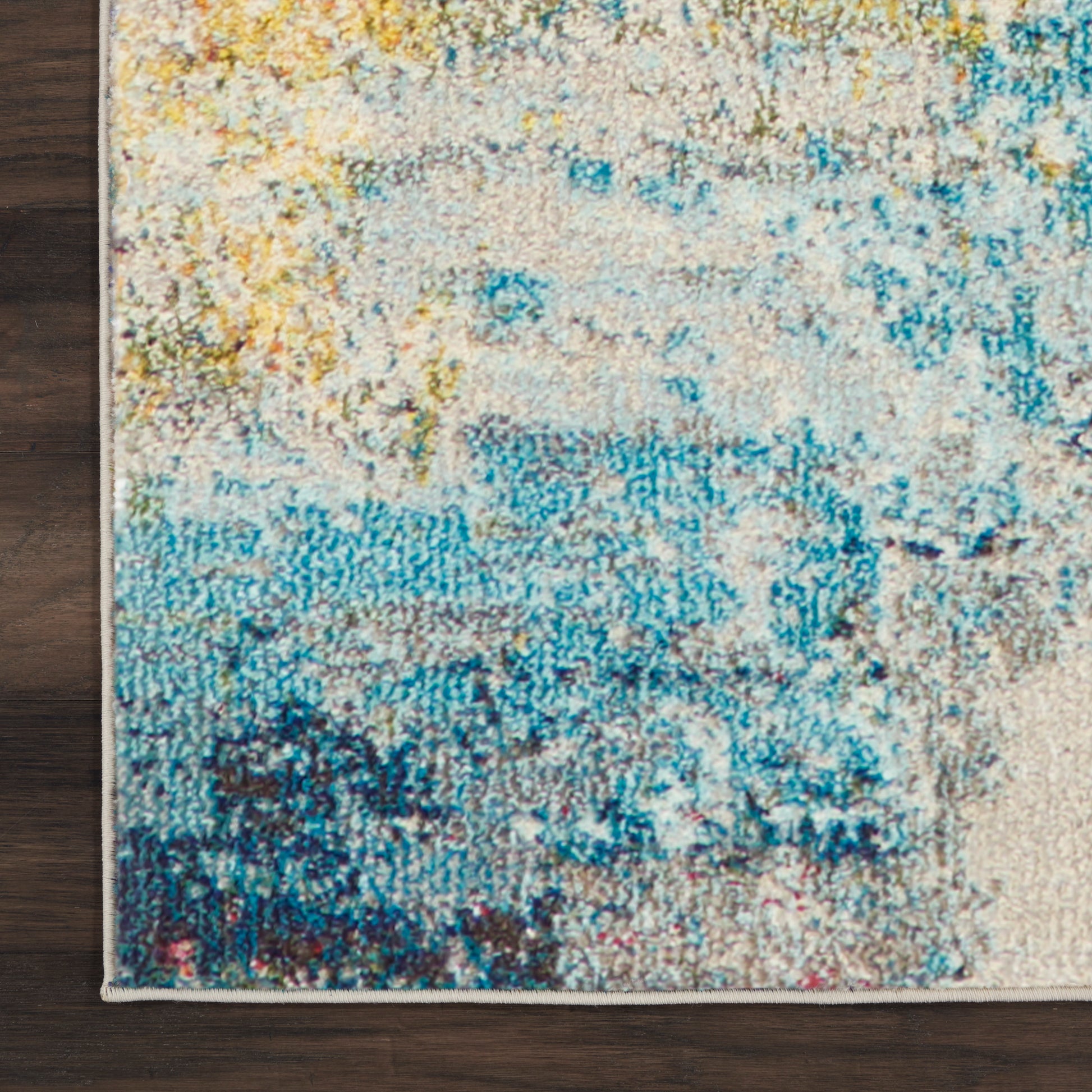Abstract rectangular area rug with blue, teal, yellow and beige hues; soft textured pile on dark hardwood.