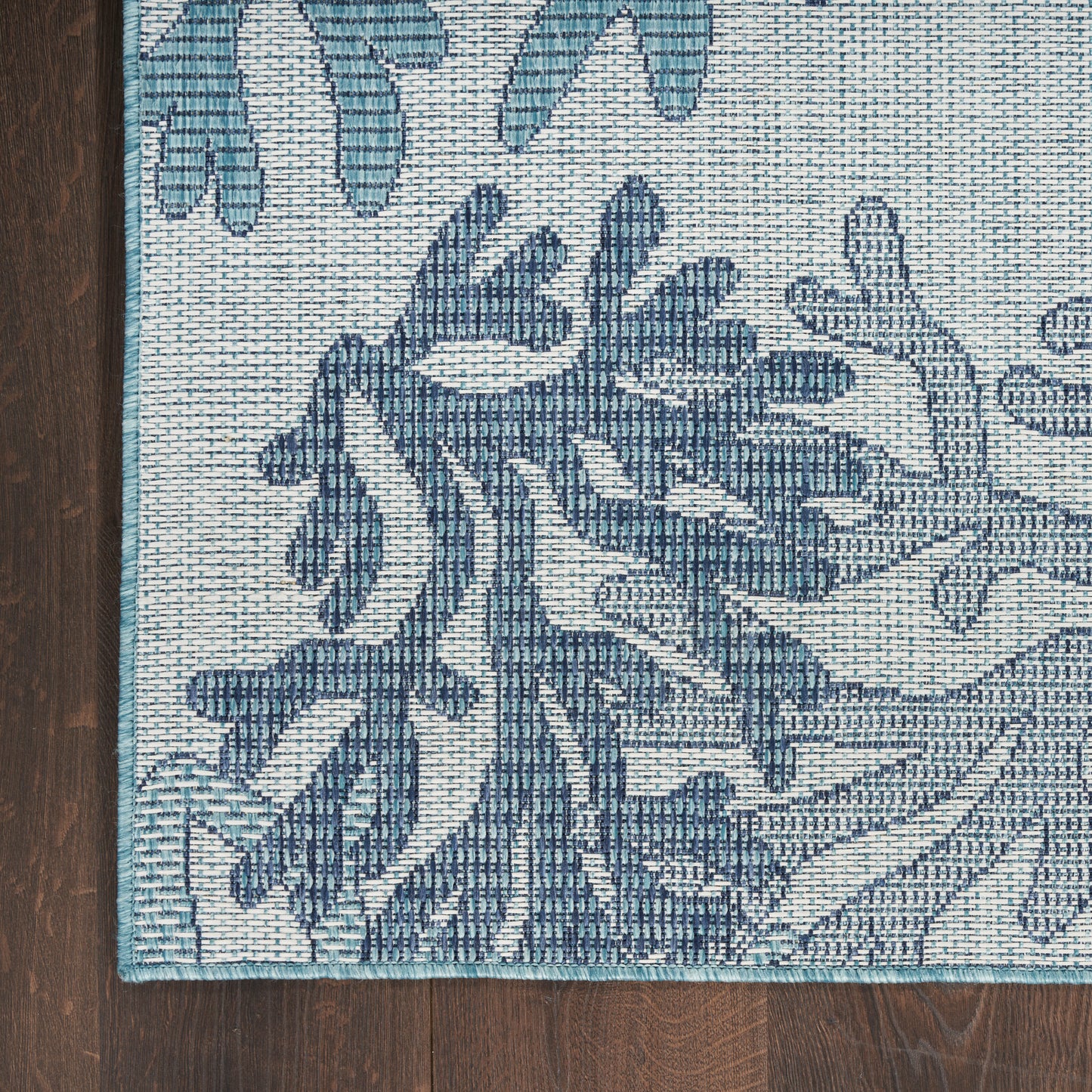 Blue-teal botanical patterned rug on ivory background, woven texture and turquoise border, corner view on dark wood floor