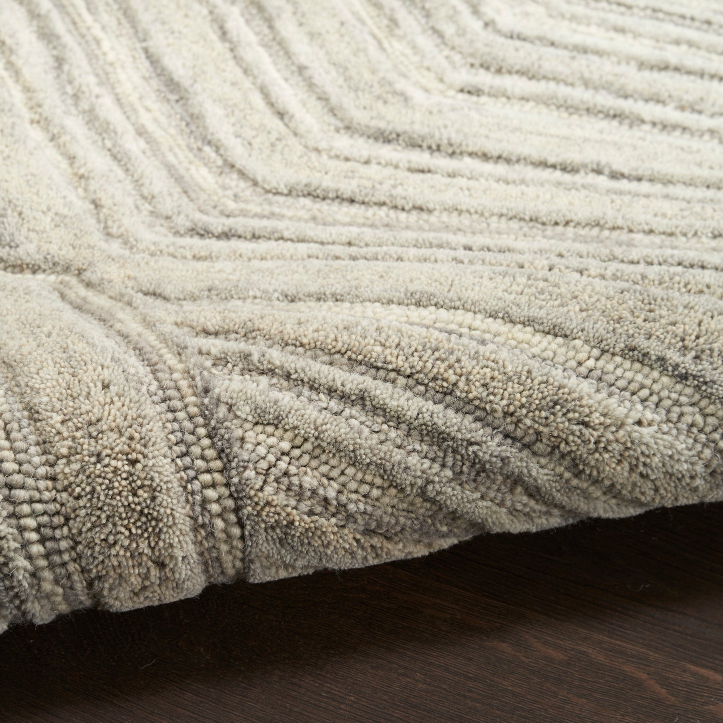 Beige shag rug with thick loop pile and subtle wave texture on dark wood floor.