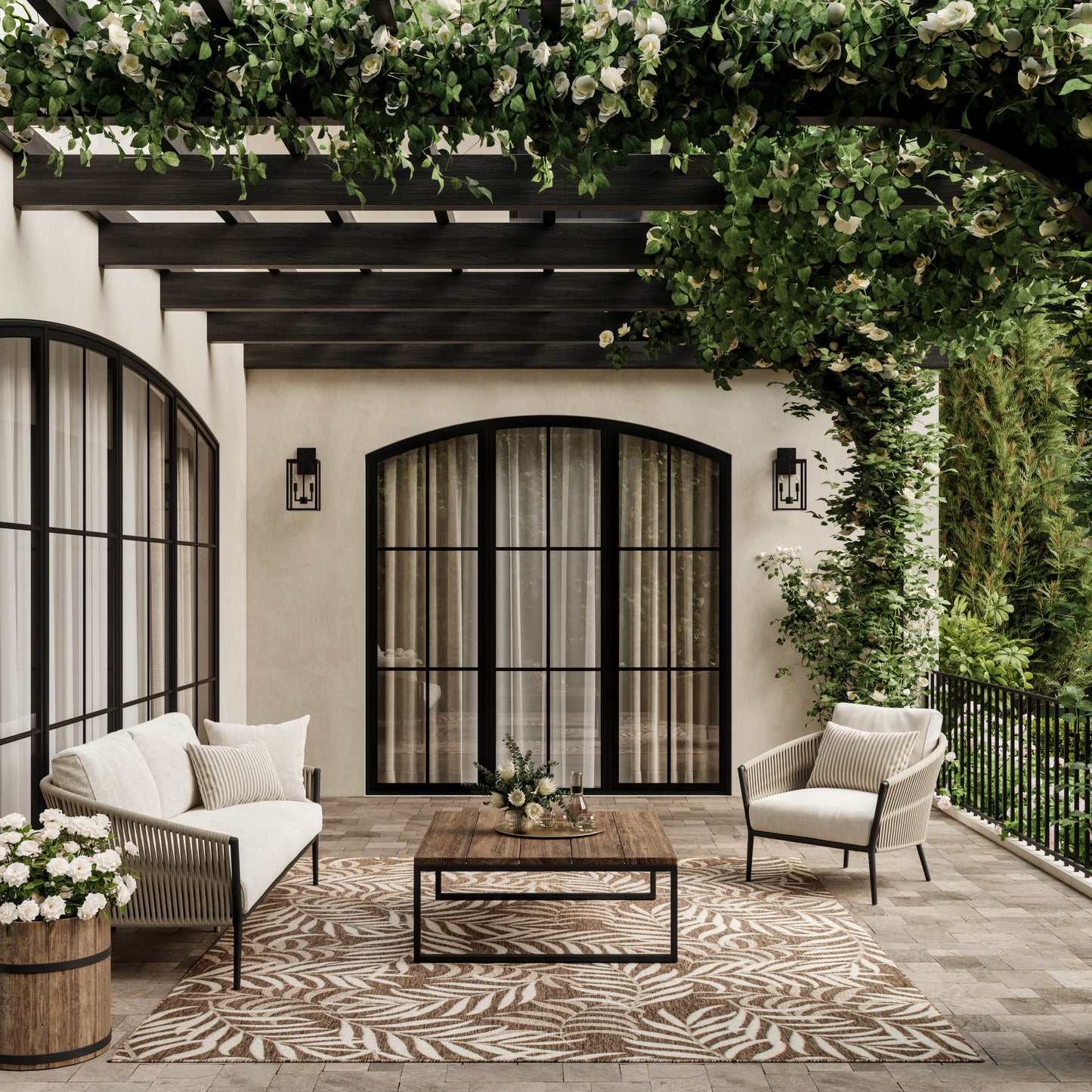 Outdoor patio with arched black-framed doors, cream cushioned seating, wooden coffee table, leaf-pattern rug, lush greenery.