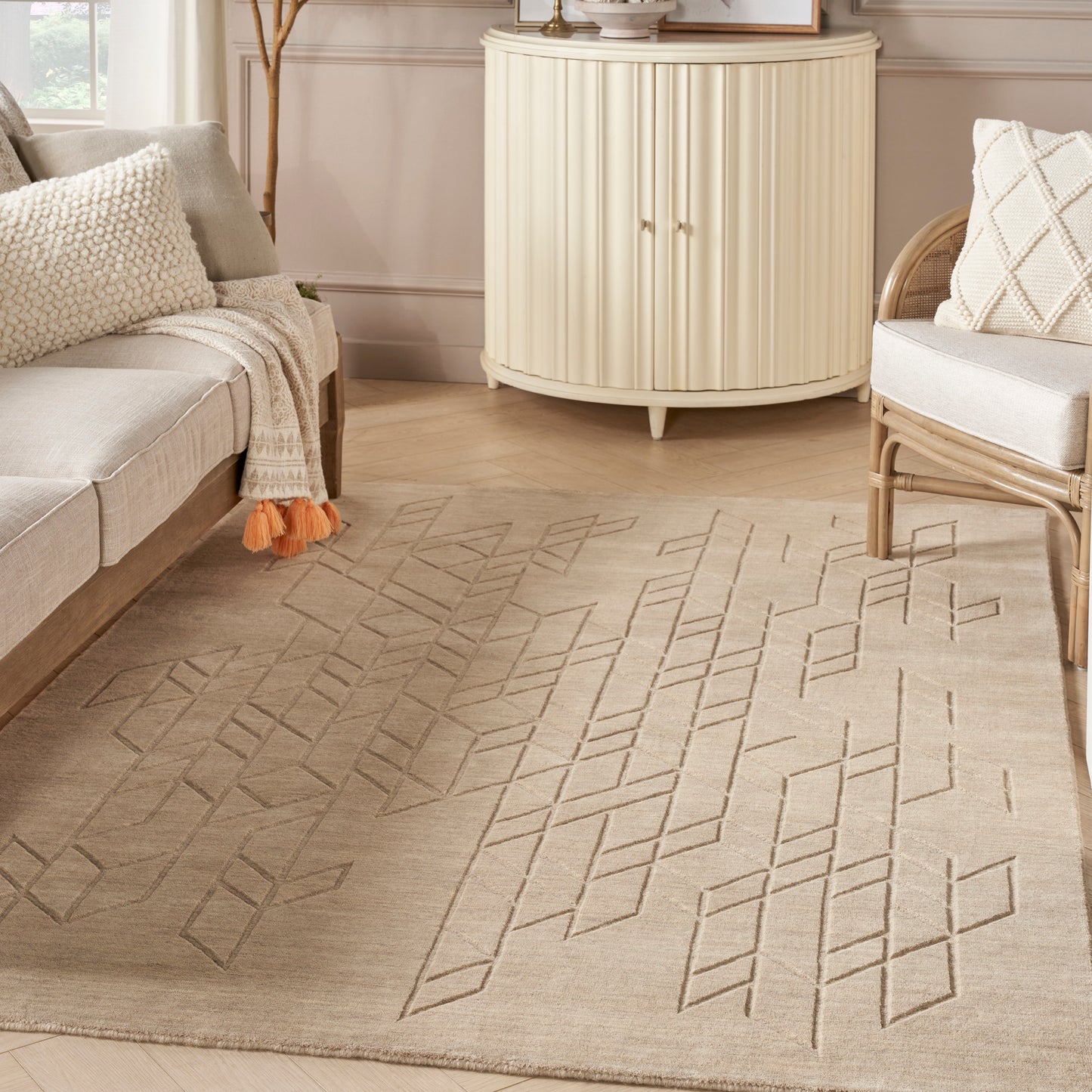 Beige geometric area rug with stitched diamond lines on light wood floor in a neutral living room with cream furniture.
