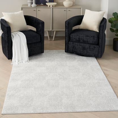 5' x 7' modern rug with a light pattern in a living room, with black velvet barrel chairs, cream cushions, and a white throw nearby.