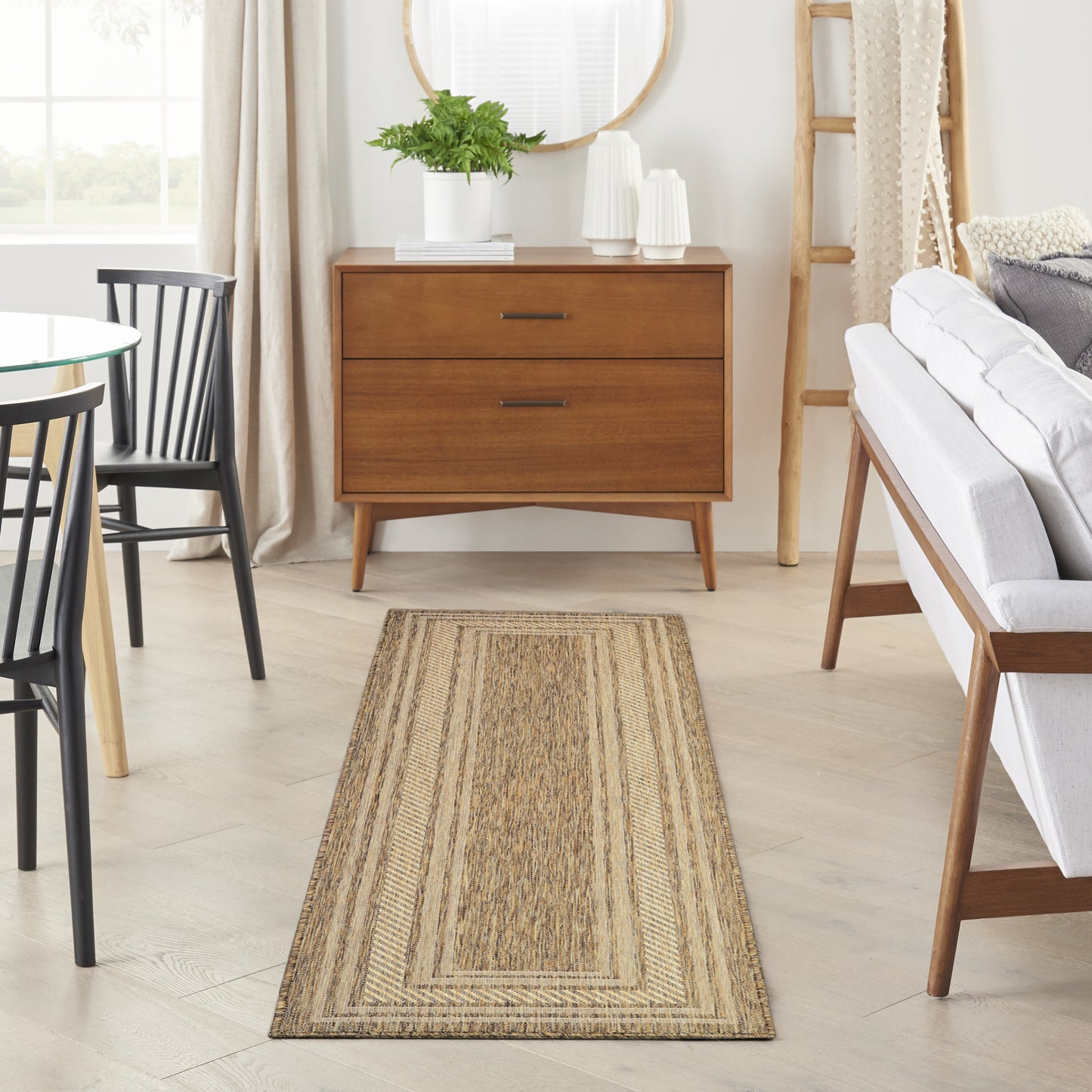 Natural woven jute rug runner on light wood floor in a mid-century living room with an oak dresser, plant & gray sofa.