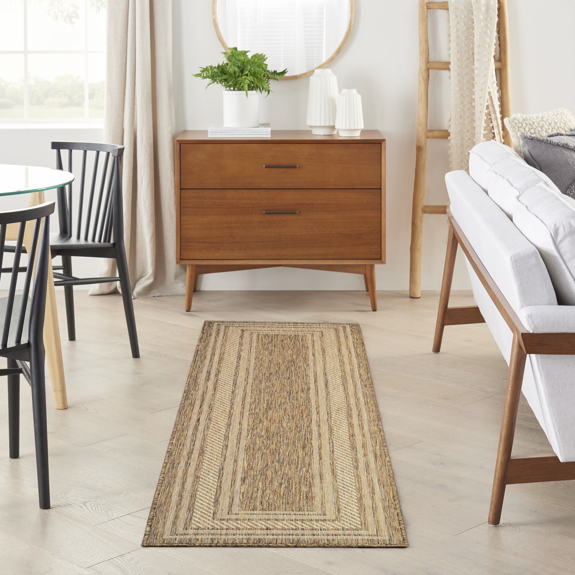 Natural woven jute rug runner on light wood floor in a mid-century living room with an oak dresser, plant & gray sofa.