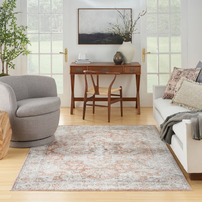 Neutral living room with a vintage patterned rug, oak desk and chair, gray round fabric chair, and beige sofa with pillows.