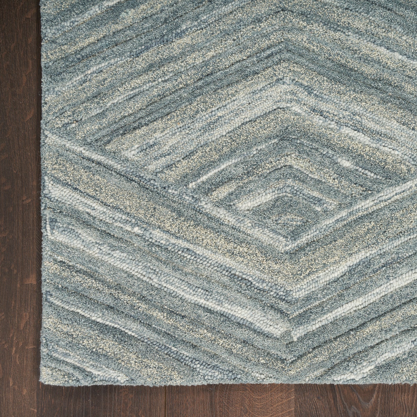 Blue-gray textured area rug with chevron diamond pattern on dark wood floor
