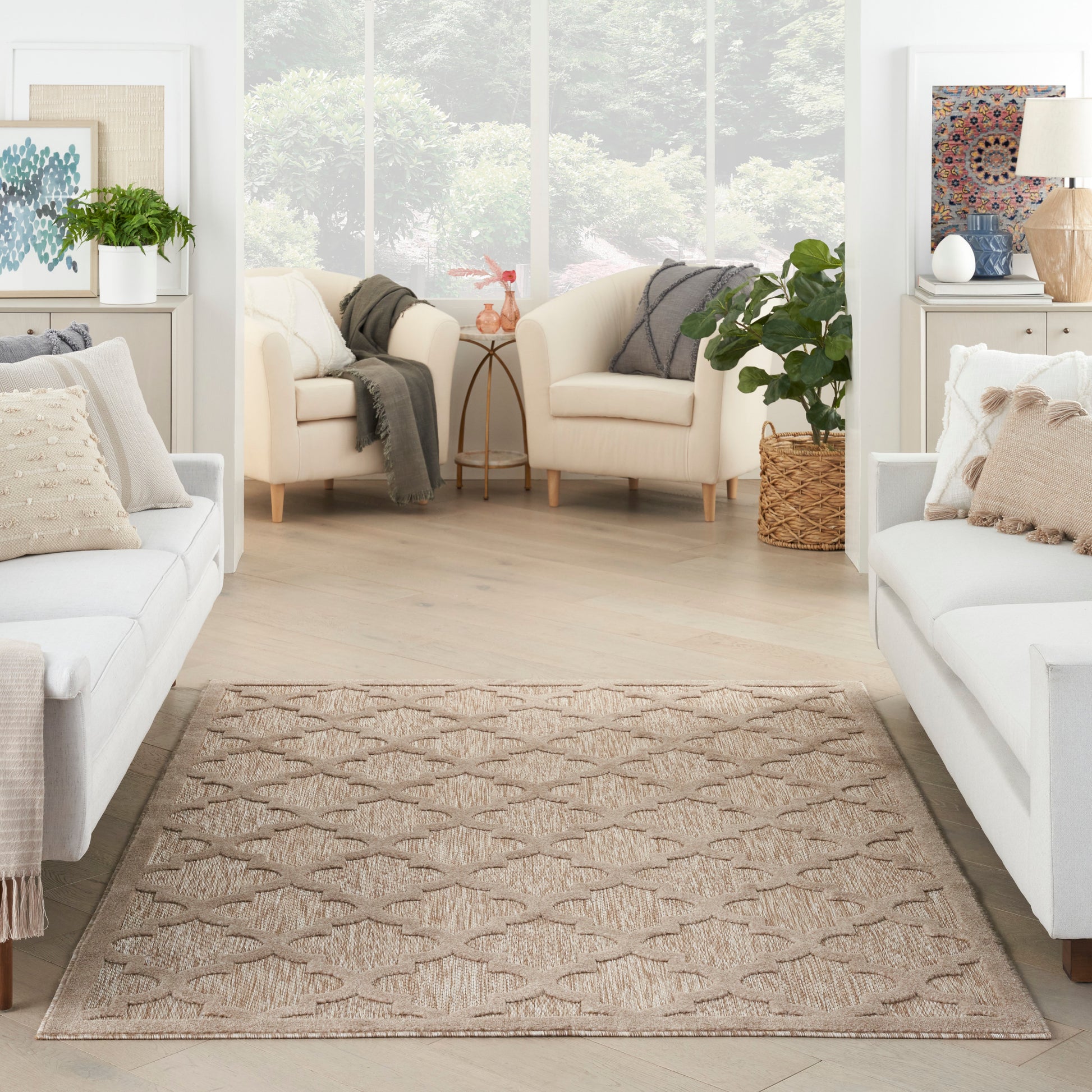 Taupe woven area rug with subtle diamond and leaf pattern in a bright living room with white sofas.
