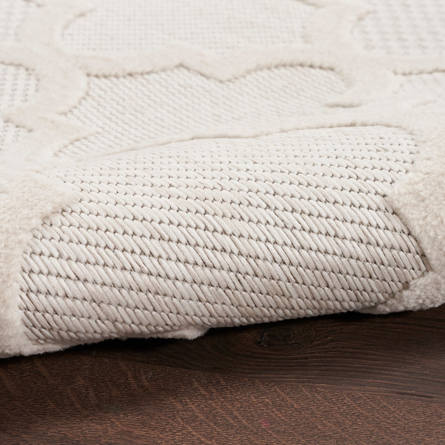 Cream textured rug with a dense twisted pile and raised scroll pattern on a dark wood floor.