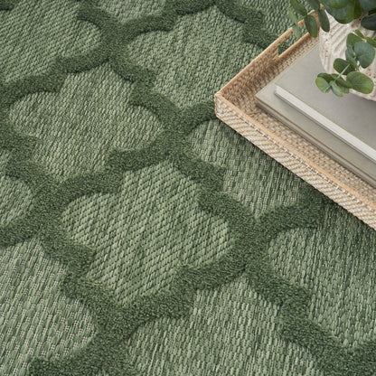 Green woven area rug with interlocking geometric pattern; wicker basket with books and a plant on edge.