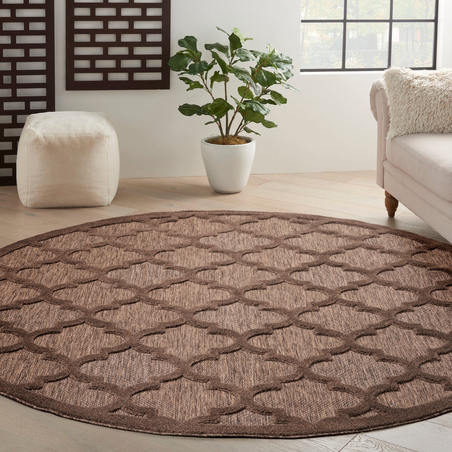 Round brown woven rug with a lattice trellis pattern on a light wood floor in a neutral living room.