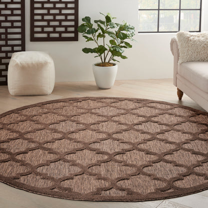 Round brown woven rug with a lattice trellis pattern on a light wood floor in a neutral living room.