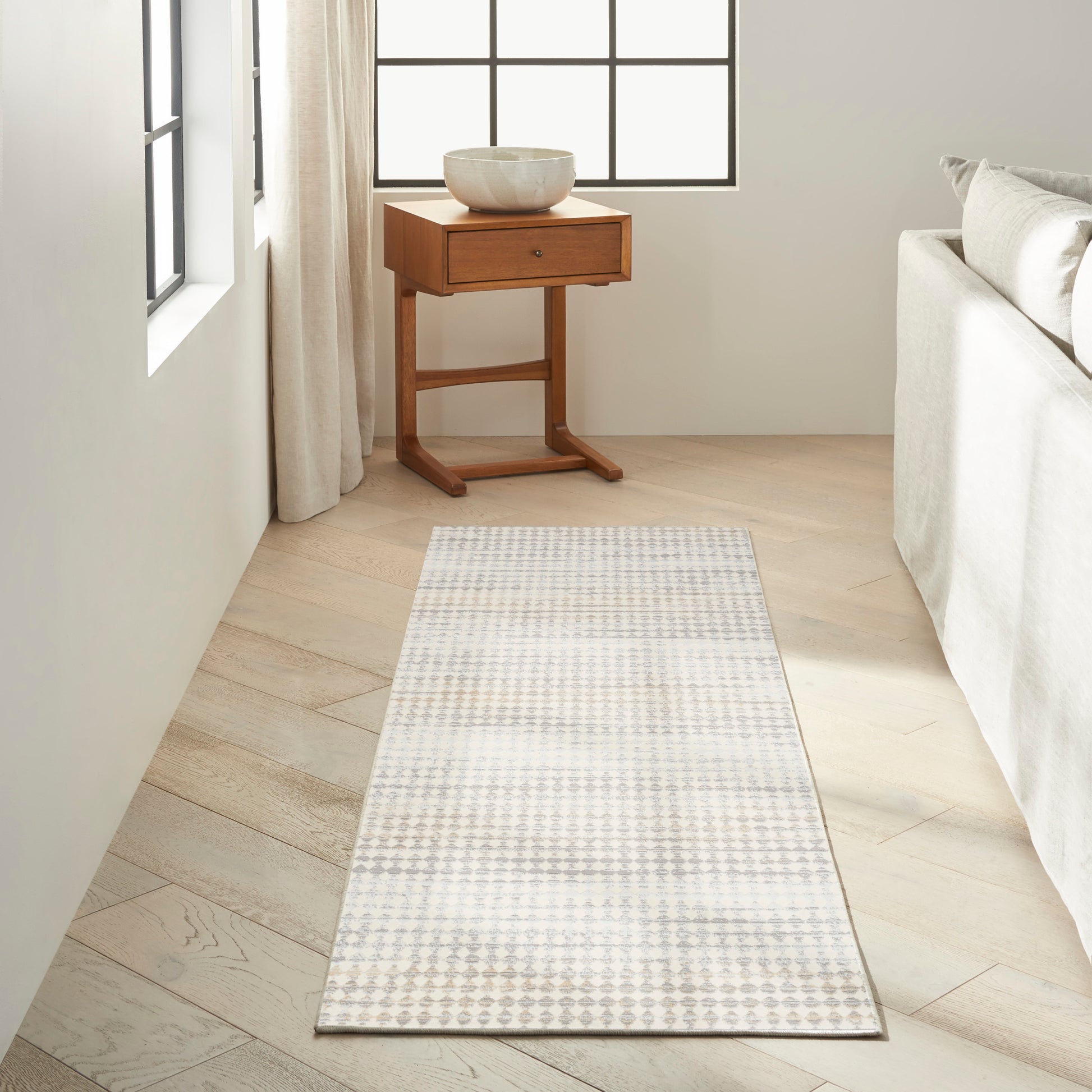 Light gray and white geometric runner rug on pale wood floor beside a wooden side table topped with a ceramic bowl.