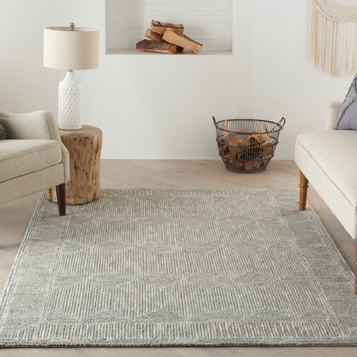 Soft gray geometric woven rug in a bright living room with beige sofa, armchair, wood stump side table, and log basket.
