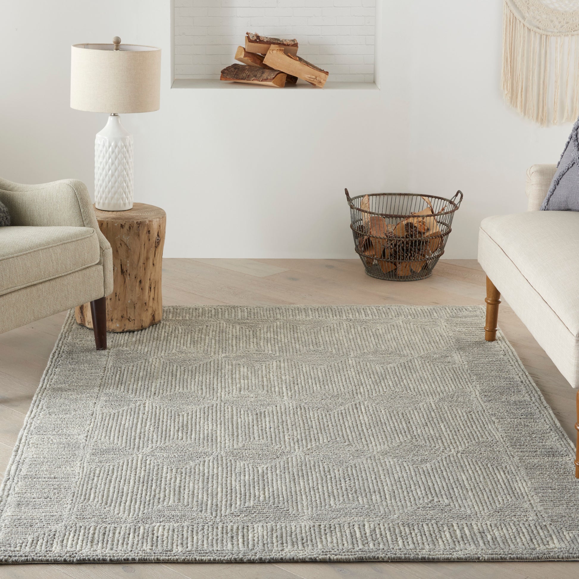 Soft gray geometric woven rug in a bright living room with beige sofa, armchair, wood stump side table, and log basket.