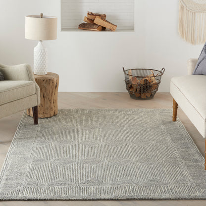 Soft gray geometric woven rug in a bright living room with beige sofa, armchair, wood stump side table, and log basket.