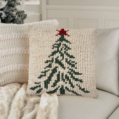 Cream chunky-knit decorative pillow featuring a green Christmas tree and red star, on a light sofa.