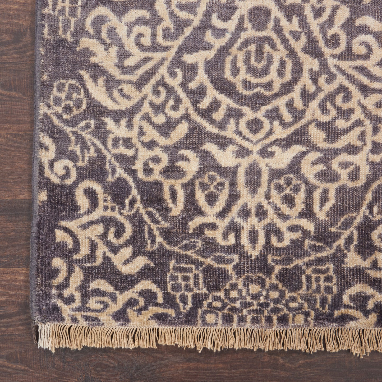 Dark indigo rug with beige oriental floral medallion pattern & fringe on wooden floor.