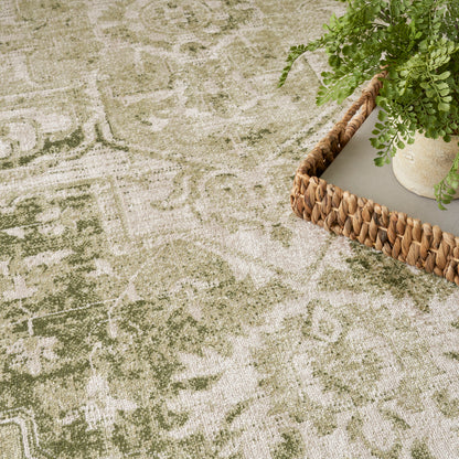 Olive and beige patterned round area rug with a soft distressed pile; woven texture and a wicker tray with a plant.