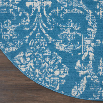 Round blue rug with distressed white damask pattern on wood floor; bound edge.