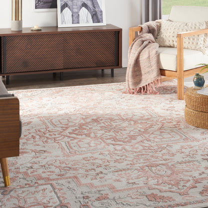 Living room with a pink patterned area rug, mid-century wood sideboard, beige sofa with knit blanket, and wicker ottoman.