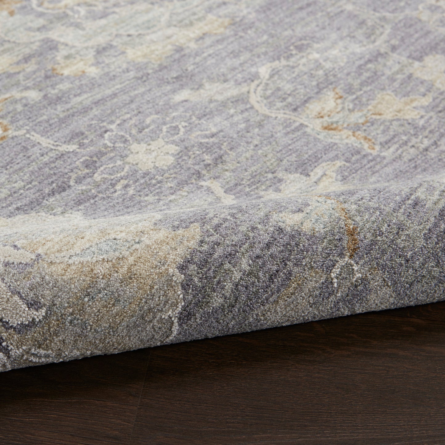 Close-up of blue-gray tufted rug with ivory floral pattern and beige accents, edge folded on dark wood floor.