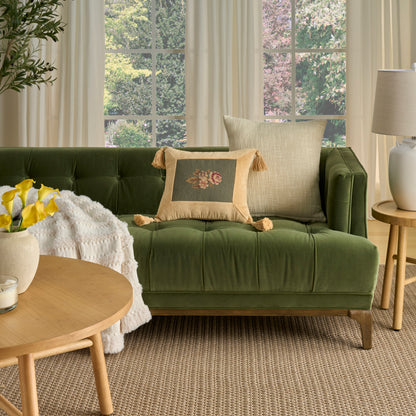 Olive green tufted velvet sofa with beige tassel cushion and cream throw, round wood coffee table with yellow flowers.