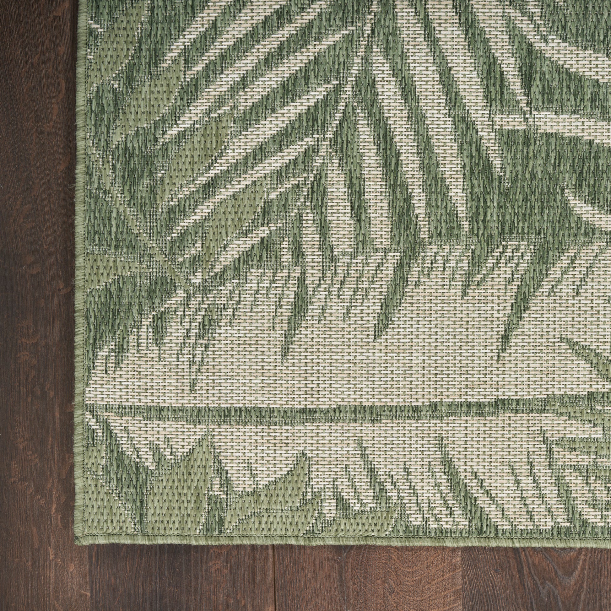 Rectangular woven rug with green palm leaf pattern on cream backdrop; olive and sage tones, bound edge.