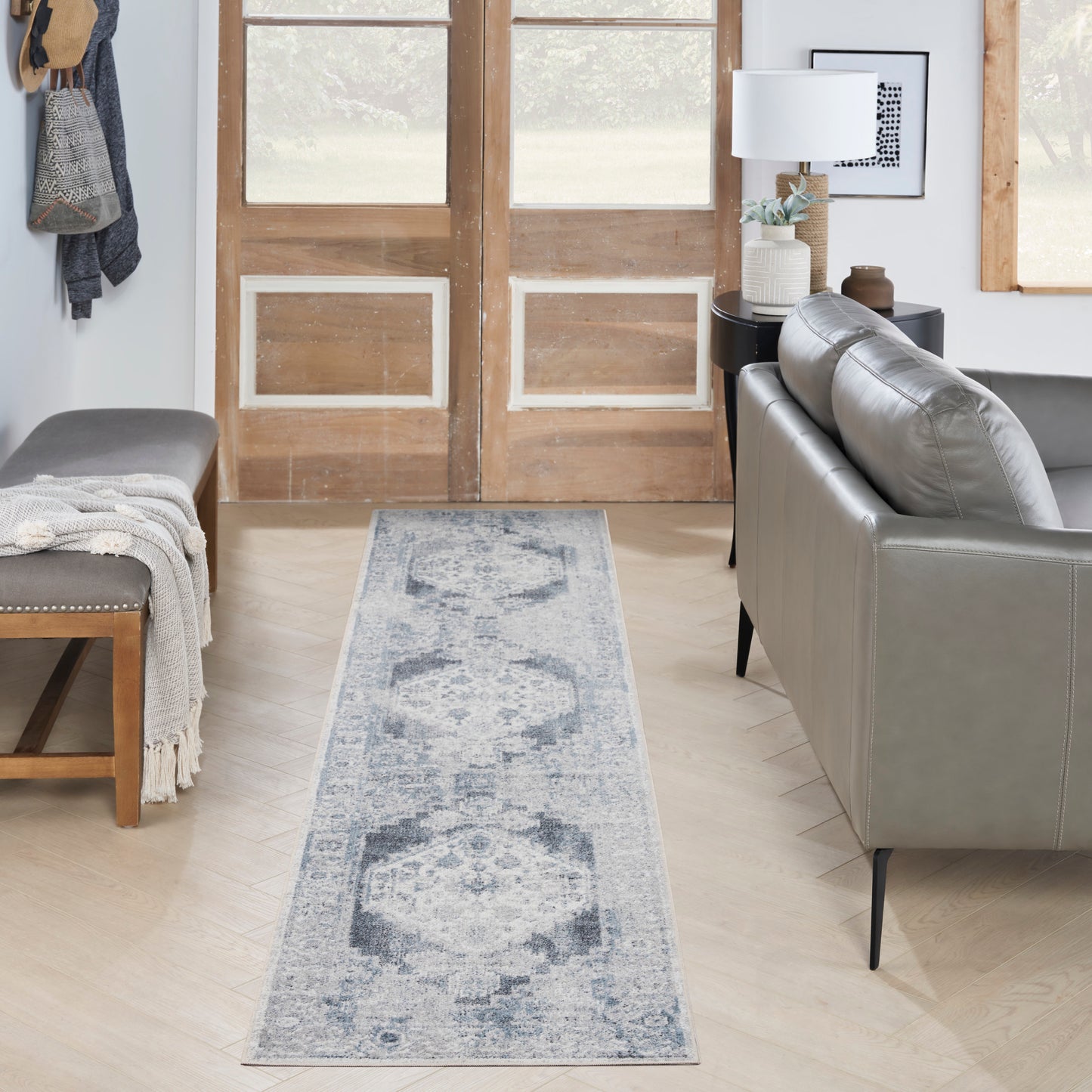 Blue-gray patterned runner rug on light wood floor in a modern rustic living room with a gray sofa, bench and wooden doors.