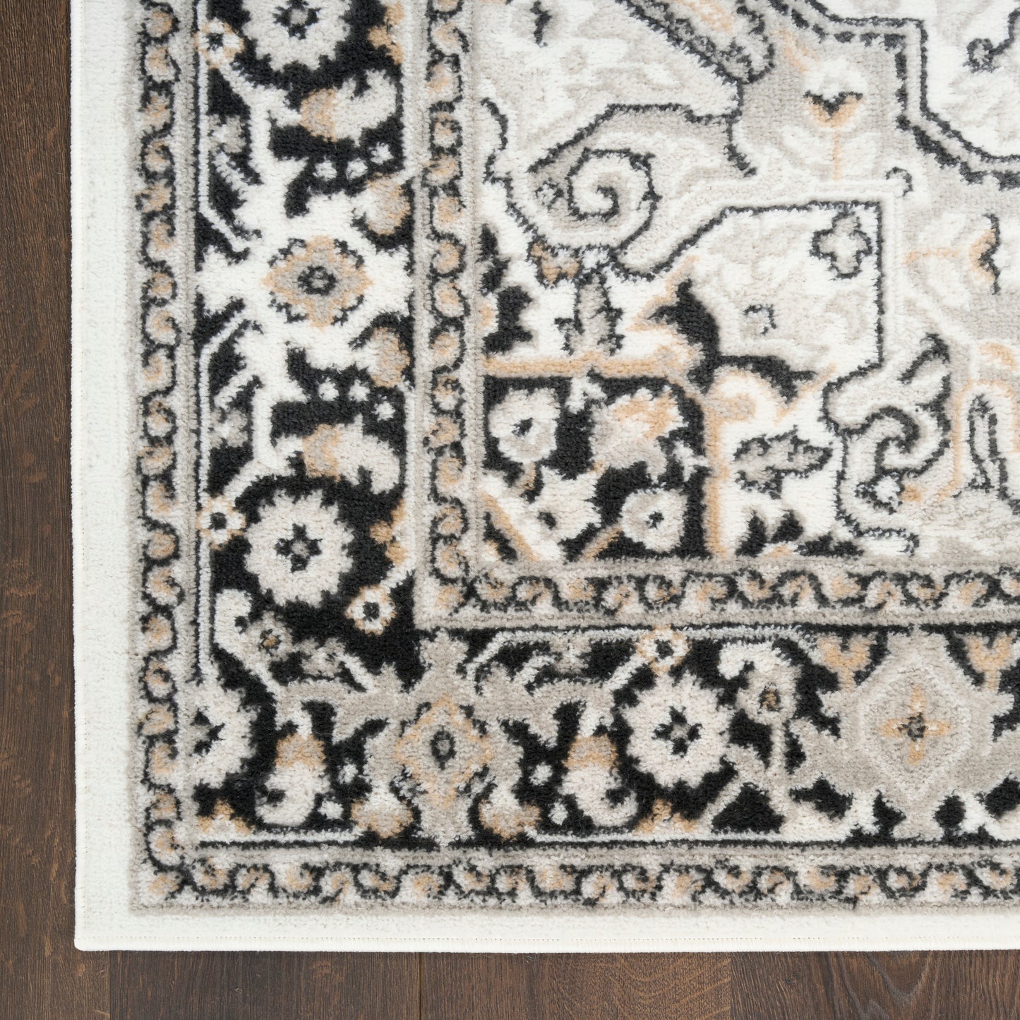 Traditional floral border rug in ivory beige and black with corner view on wood floor.